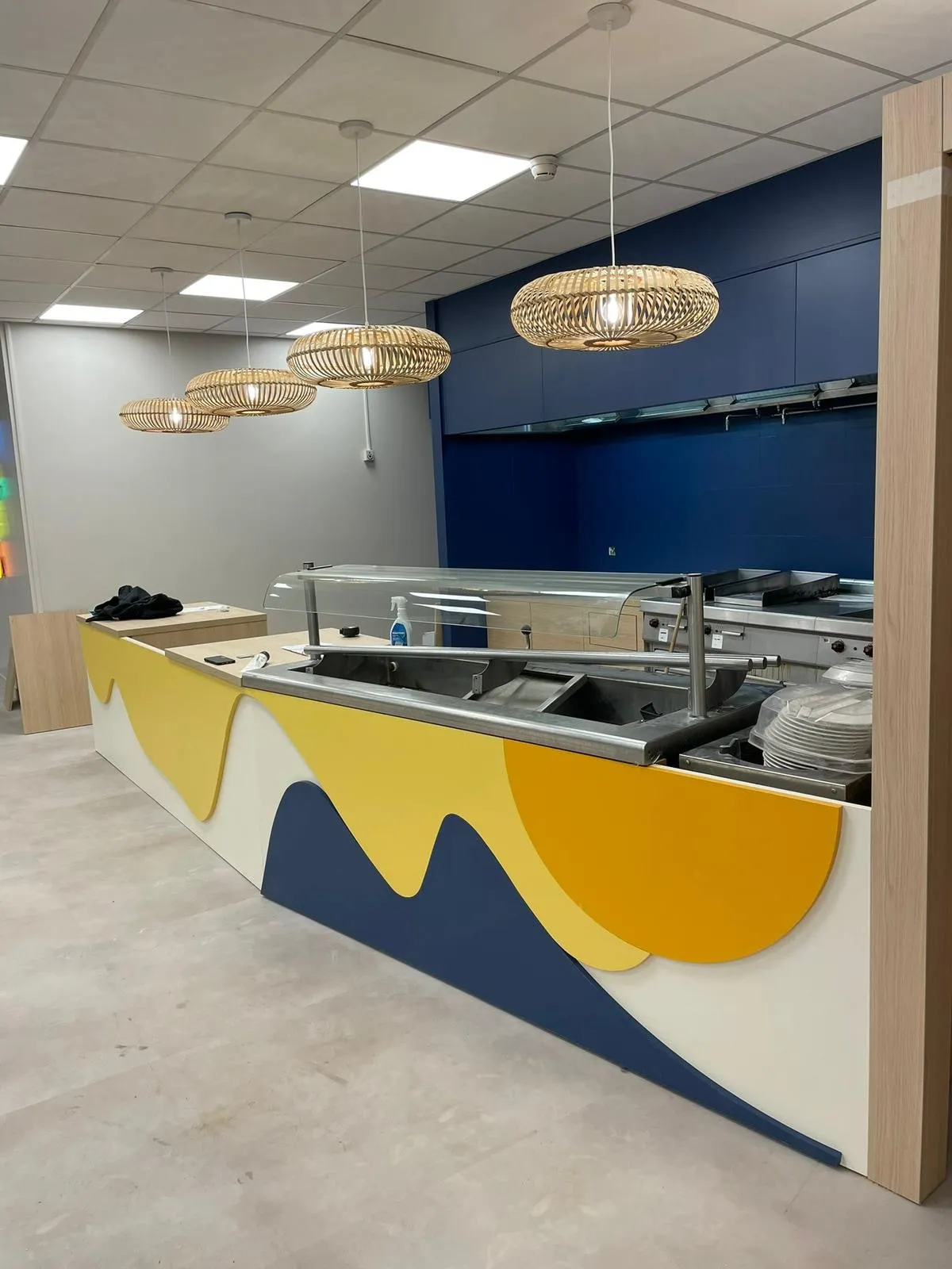 Ligne de self avec façade décorative jaune bleu et blanc, vitrine chauffante inox et bandeau bleu marine