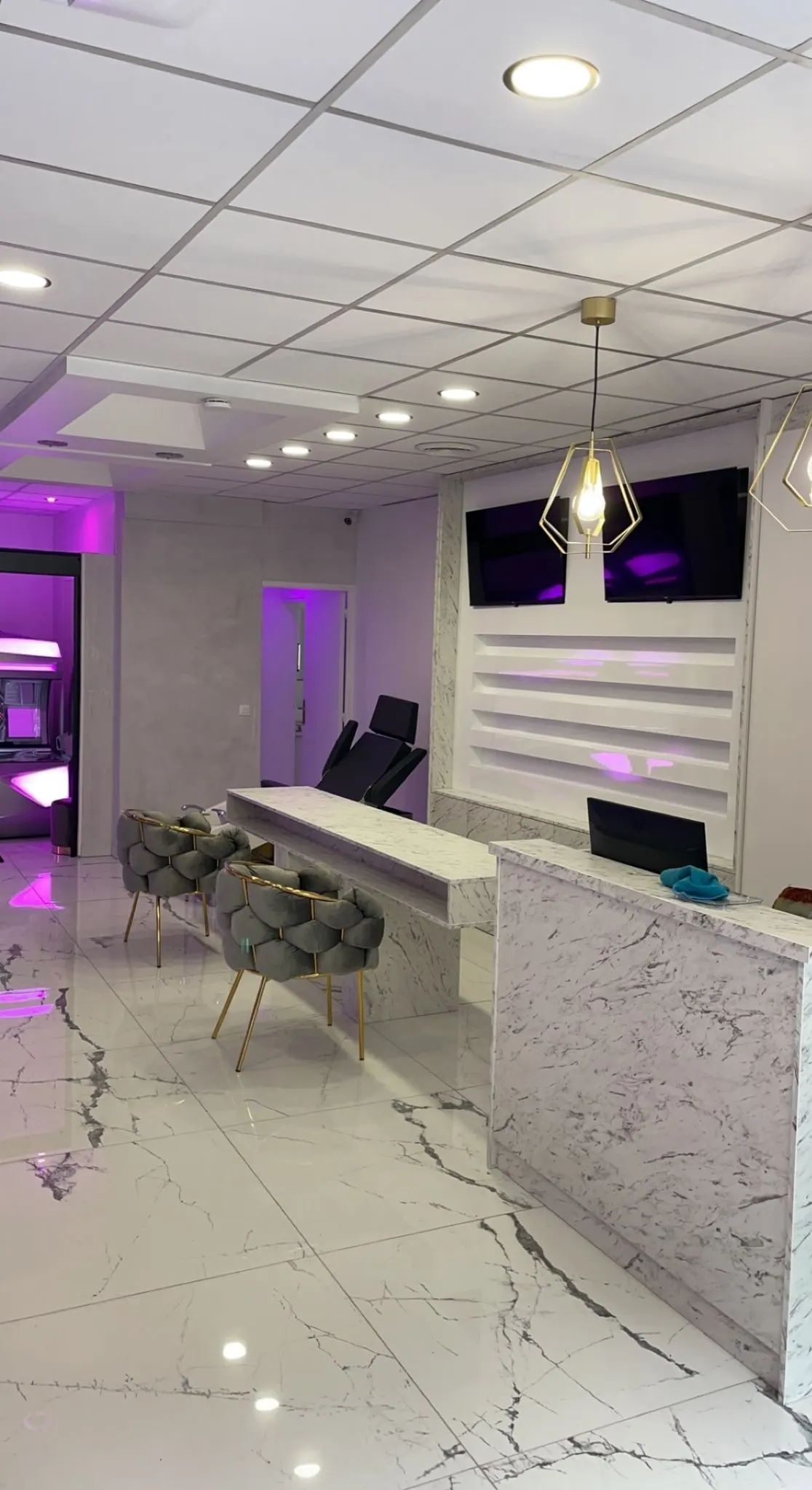 Banque d’accueil en décor marbre avec tablette haute, mur d’étagères éclairé et écrans