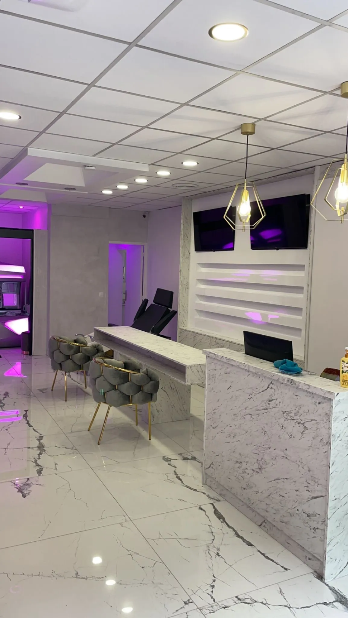 Banque d’accueil en décor marbre avec tablette haute, mur d’étagères éclairé et écrans