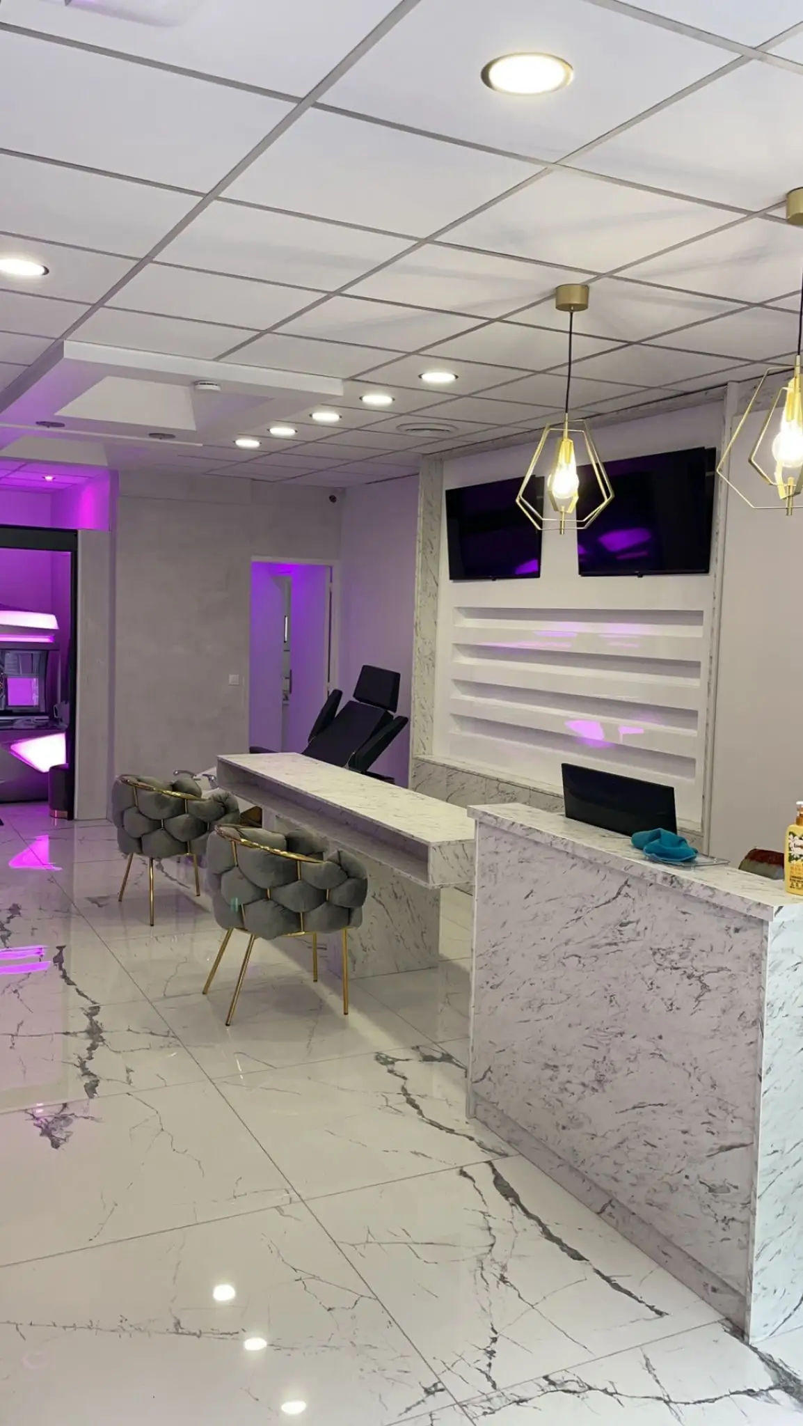 Banque d'accueil en décor marbre avec tablette haute, mur d'étagères eclaire et ecrans