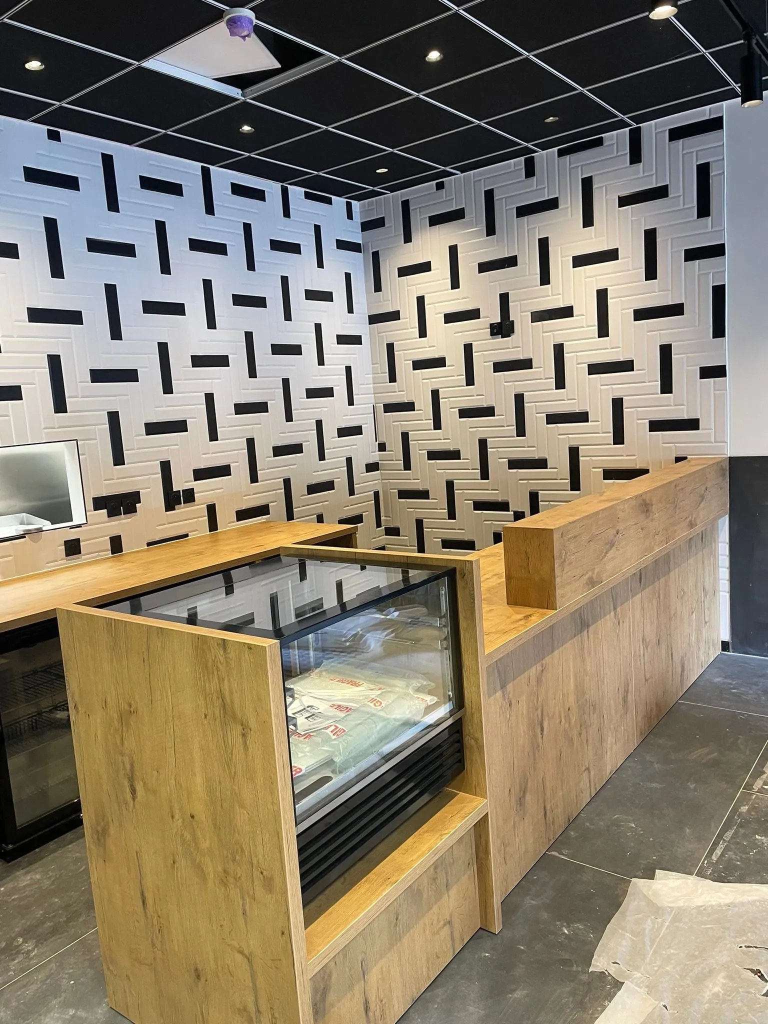 Comptoir en L chêne clair avec vitrine réfrigérée encastrée et retour surelevé, mur faïence blanche a relief