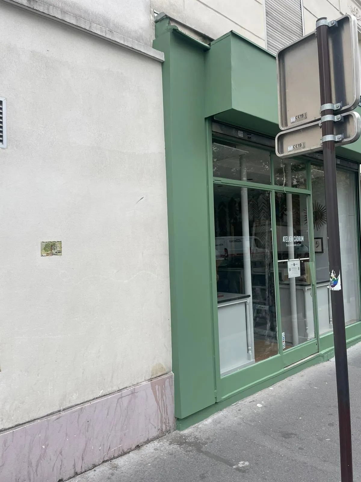 Devanture verte en angle de rue avec bandeau haut, vitrine et porte vitrée d’un atelier d’encadrement