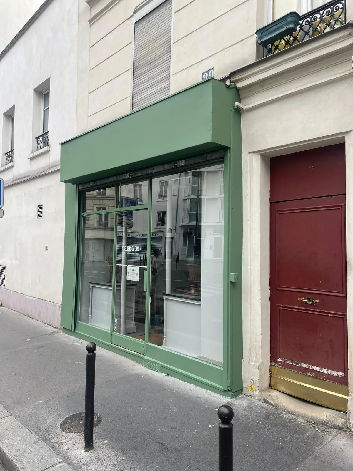 Devanture de commerce vert amande vue de face, vitrine coulissante et porte d’immeuble rouge à côté