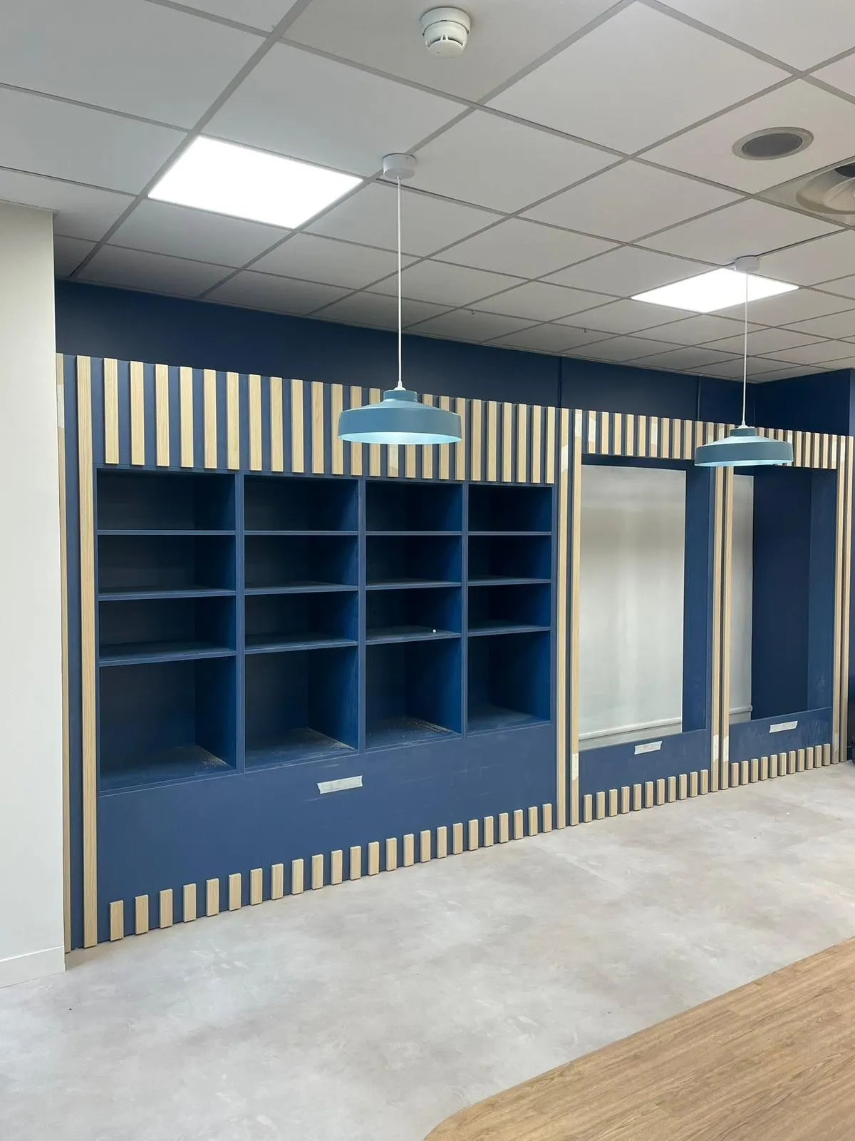 Mur bleu marine avec casiers ouverts et habillage en tasseaux de bois clair, suspensions bleues