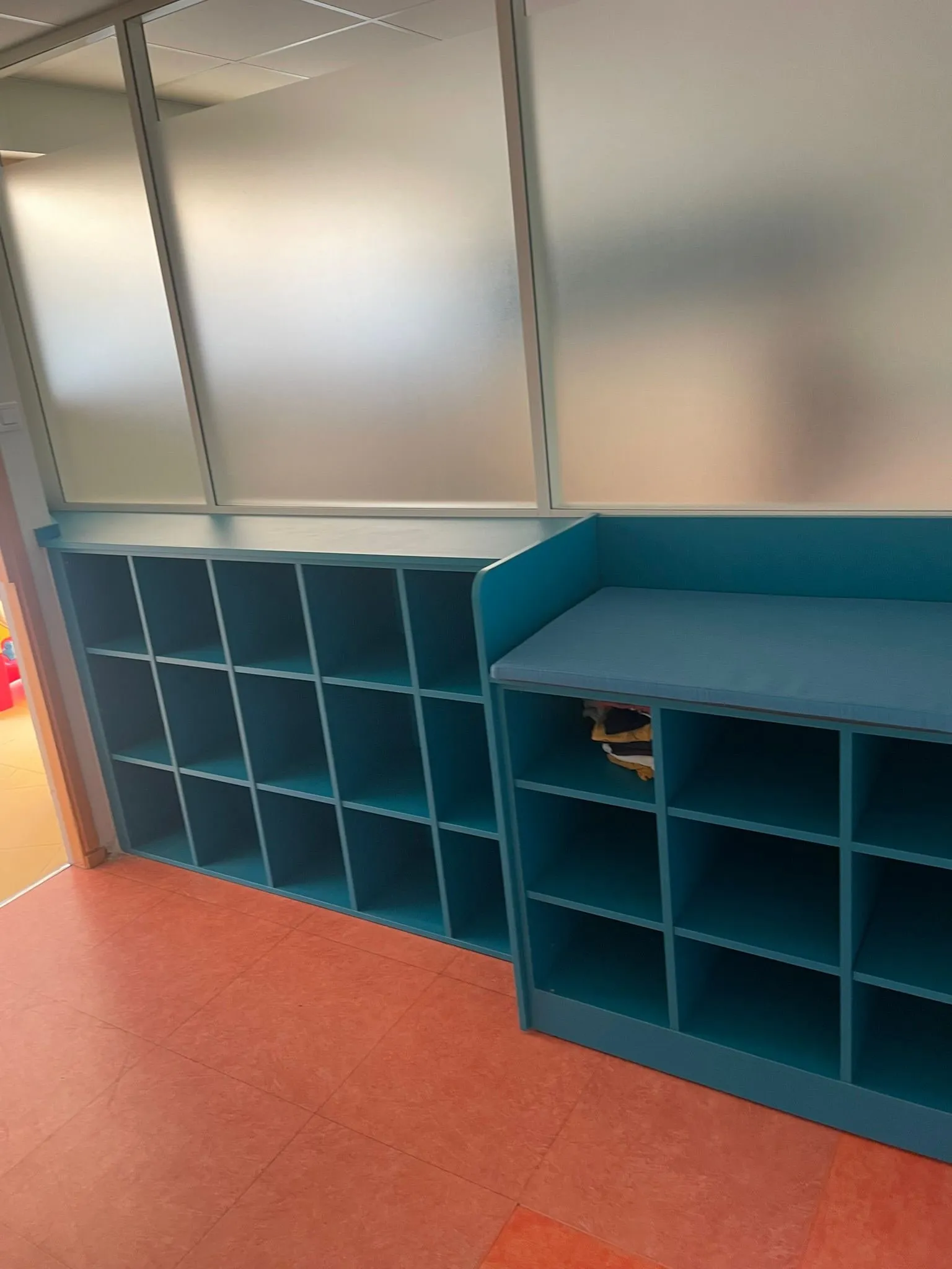 Casiers a cases bleu canard et banc a assise sous cloison vitrée depolie, sol linoleum orange