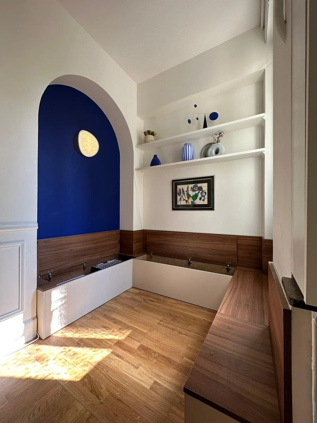 Banquette d angle a coffres en décor noyer et blanc sous une niche voutee peinte en bleu, étagères murales blanches