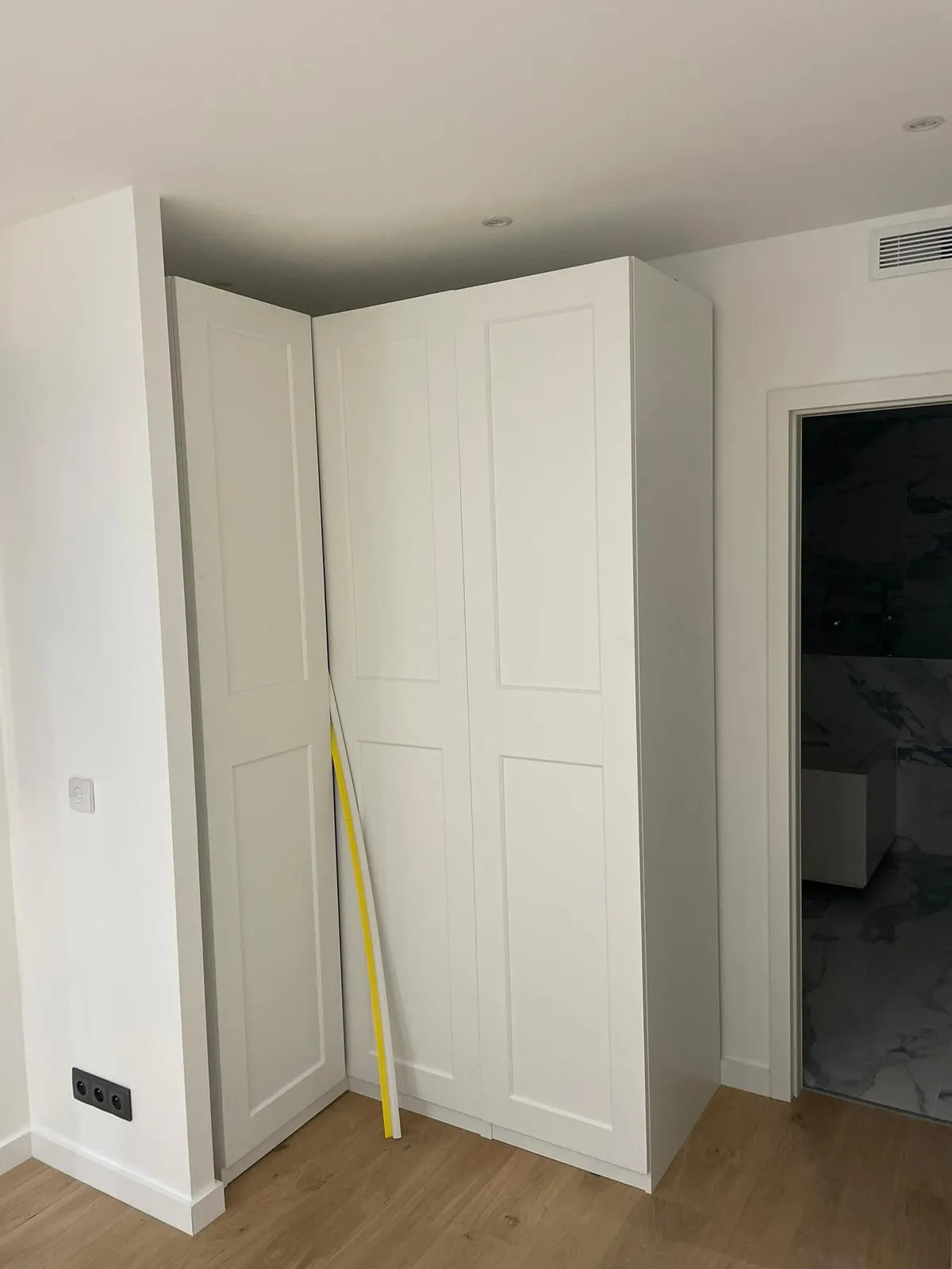 Placard d angle blanc a portes cadre pose du sol au plafond, a cote de l entree d une salle de bain