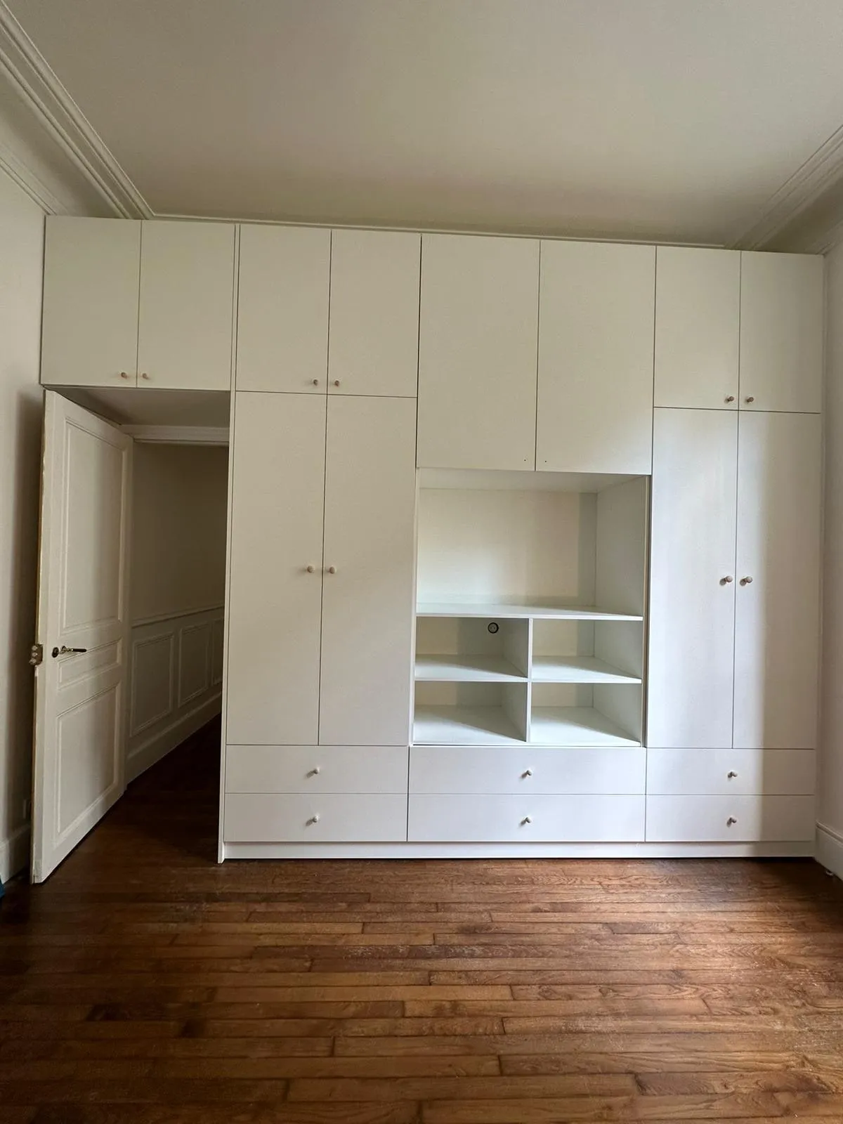 Placard blanc toute hauteur avec niche centrale a casiers, tiroirs bas et boutons bois, parquet ancien