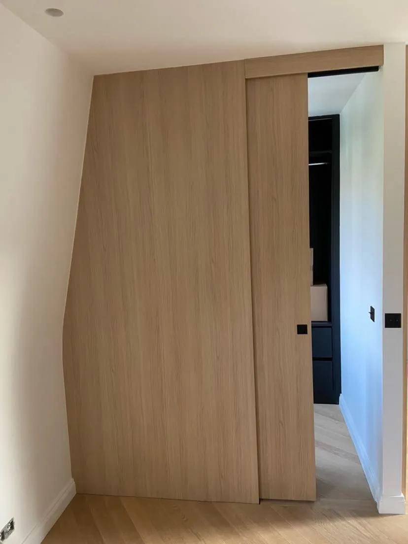Porte coulissante plaquée chêne à chant courbe, encastrée dans un habillage mural assorti