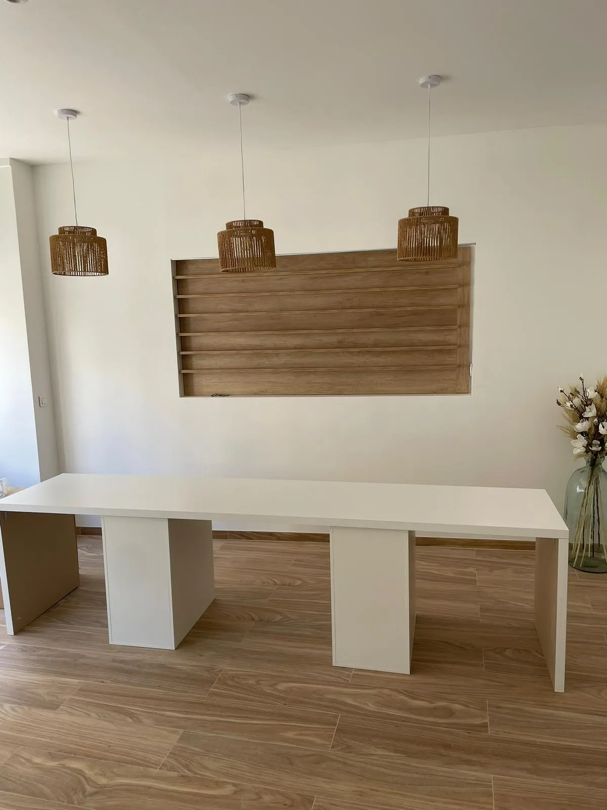 Grande table blanche sur pieds panneaux et panneau mural décor bois a tablettes, trois suspensions en fibre